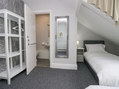 A bedroom with a single bed a bedside table with lamp a wall mirror and an open door to a small bathroom at Park Beck 3 Windermere
