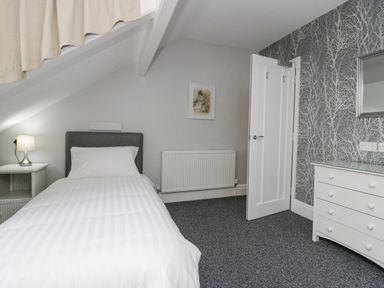 A bedroom with a single bed a bedside table with a lamp a chest of drawers and a door at Park Beck 3 in Windermere