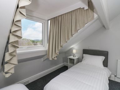 A small bedroom with a single bed a bedside table and a lamp under a sloped ceiling with a window and curtains at Park Beck 3 in Windermere