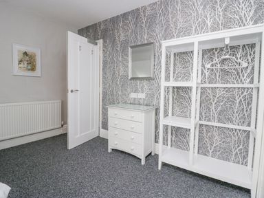 A room with a chest of drawers an open wardrobe a wall mirror and a door at Park Beck 3 Windermere