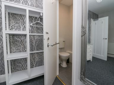 A wardrobe with hangers a partially open door showing a toilet and a mirror reflecting a door and a chest of drawers at Park Beck 3 in Windermere