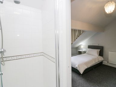 A tiled shower area next to a bedroom with a single bed a bedside table lamp and a radiator at Park Beck 3 in Windermere