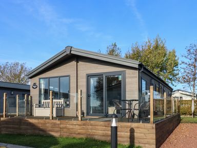 A wooden lodge with a glass railing deck and outdoor table with chairs at Brocklebank Lodge 35 High Hesket near Armathwaite
