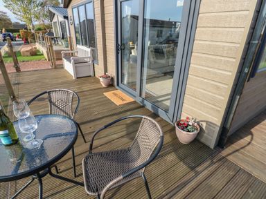 An outdoor deck with a glass table and two wicker chairs at Brocklebank Lodge 35 in High Hesket near Armathwaite