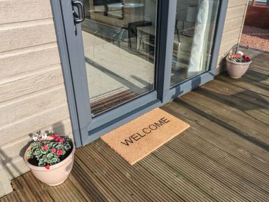 A glass door entrance with a welcome mat and two flower pots on a wooden deck at Brocklebank Lodge 35 High Hesket near Armathwaite