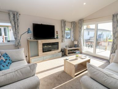 A living room with two sofas a wooden coffee table a TV on a stand and windows with curtains at Brocklebank Lodge 35 High Hesket near Armathwaite