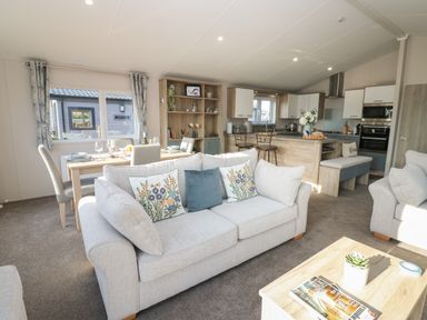 An open living area with sofas, a dining table, bookshelves, and a kitchen at Brocklebank Lodge, 35 in High Hesket near Armathwaite