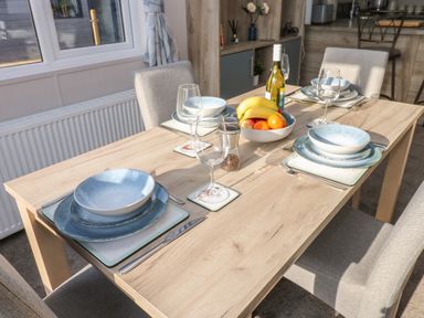 A dining table set with plates bowls glasses and cutlery with a fruit bowl and wine bottle in a dining room at Brocklebank Lodge 35 High Hesket near Armathwaite