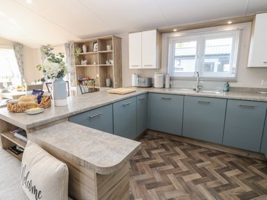A kitchen with blue lower cabinets white upper cabinets and a window above the sink at Brocklebank Lodge 35 in High Hesket near Armathwaite