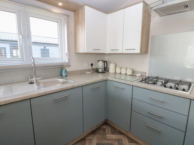 A kitchen with a sink under a window a kettle and containers on the counter and a gas stove at Brocklebank Lodge 35 High Hesket near Armathwaite