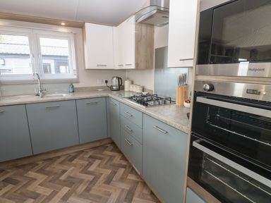 A kitchen with grey lower cabinets white upper cabinets a gas stove an oven microwave a kettle and a window at Brocklebank Lodge 35 High Hesket near Armathwaite