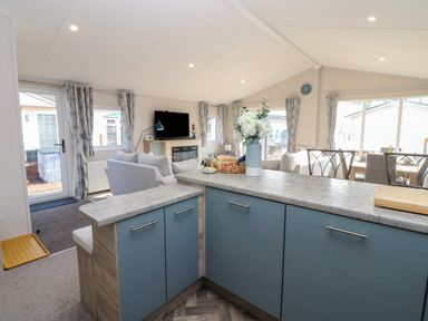 An open plan living area with a blue kitchen island flowers in a vase grey sofas a television and dining table at Brocklebank Lodge 35 High Hesket near Armathwaite
