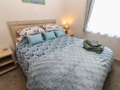 A bedroom with a bed with floral bedding and pillows a bedside table with a lamp and a window with curtains at Brocklebank Lodge 35 High Hesket near Armathwaite