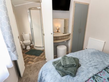 A bedroom with a bed and stacked towels next to a small bathroom with a shower and toilet at Brocklebank Lodge 35 High Hesket near Armathwaite