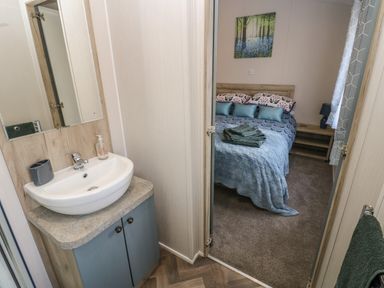 A bathroom sink with mirror and a glimpse of a bedroom with a bed and bedside table at Brocklebank Lodge 35 in High Hesket near Armathwaite