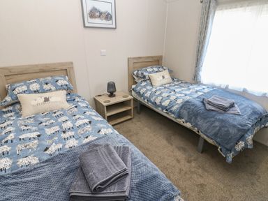 A bedroom with two single beds with sheep patterned bedding and a nightstand with a lamp in between at Brocklebank Lodge 35 High Hesket near Armathwaite