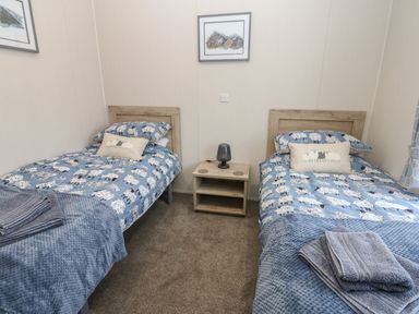 A bedroom with two single beds with sheep-themed bedding and a wooden nightstand between them at Brocklebank Lodge 35 High Hesket near Armathwaite