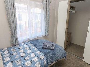 A bedroom with a bed covered in a sheep-patterned blanket and towels on top next to a window and open closet at Brocklebank Lodge 35 High Hesket near Armathwaite