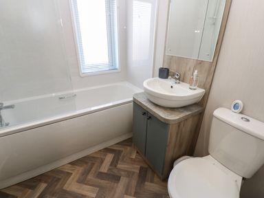 A bathroom with a bathtub next to a window a sink with cabinet a mirror above and a toilet at Brocklebank Lodge 35 High Hesket near Armathwaite