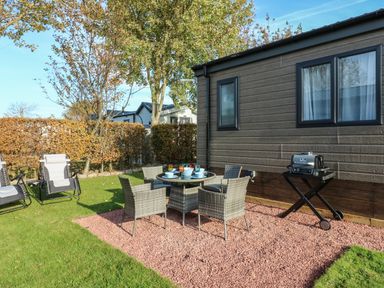 An outdoor patio area with a round table and four chairs a barbecue grill and two reclining chairs on a lawn at Brocklebank Lodge 35 High Hesket near Armathwaite