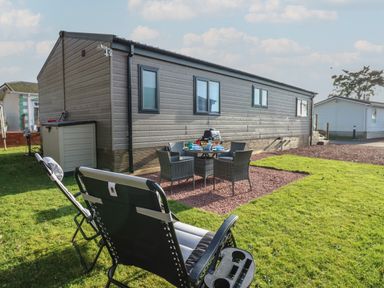 Outdoor patio area with chairs, a table set with dishes, a barbecue grill, and a mobile home at Brocklebank Lodge, 35 in High Hesket near Armathwaite