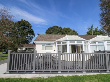 An outdoor patio with a table and chairs behind a grey fence attached to a single-story house with a conservatory at Trem-Yr-Afon in Aberaeron