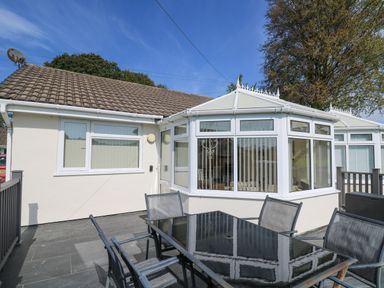 An outdoor patio with a black glass table and chairs next to a house with white walls and a windowed conservatory at Trem-Yr-Afon in Aberaeron