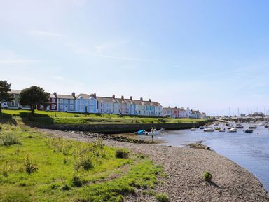 A riverside with pebble shore grass and colorful houses in the background at Trem-Yr-Afon in Aberaeron