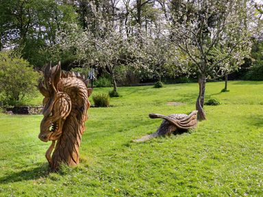 An outdoor garden with trees and wooden dragon sculptures on the grass at Trem-Yr-Afon in Aberaeron