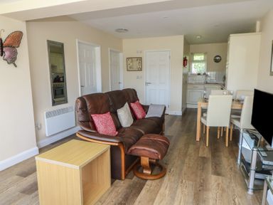A living area with a brown leather sofa and matching footstool a wooden side table a dining table with four chairs and a kitchen area at Trem-Yr-Afon in Aberaeron