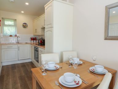 A kitchen with white cabinets and a wooden dining table set with plates bowls and glasses at Trem-Yr-Afon in Aberaeron