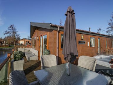 A wooden deck with outdoor seating a table an umbrella and a hot tub at The Three Bears Lodge Coniston Drive 11 South Lakeland Leisure Village near Warton