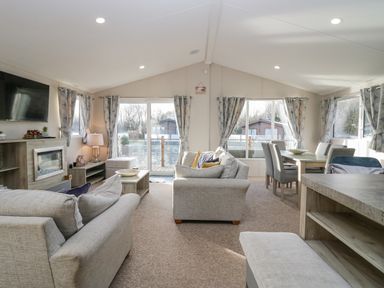 A living room with sofas, a TV, a fireplace, a coffee table, and a dining table with chairs at The Three Bears Lodge Coniston Drive 11 South Lakeland Leisure Village near Warton