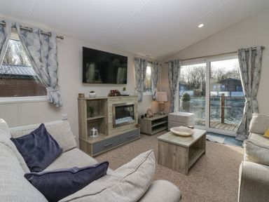 A living room with sofas a wall-mounted TV a fireplace a coffee table and sliding glass doors at The Three Bears Lodge Coniston Drive 11 South Lakeland Leisure Village near Warton