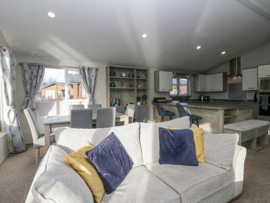 An open living room and kitchen with a sofa dining table chairs and kitchen island at The Three Bears Lodge Coniston Drive 11 South Lakeland Leisure Village near Warton