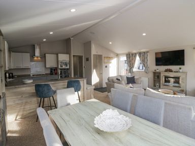 An open-plan living area with a dining table, kitchen with bar stools, sofas, fireplace, and television at The Three Bears Lodge Coniston Drive 11 South Lakeland Leisure Village near Warton