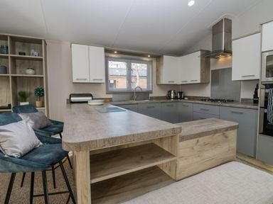 A kitchen with an island countertop and two upholstered bar stools at The Three Bears Lodge Coniston Drive 11 South Lakeland Leisure Village near Warton