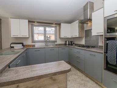 A kitchen with gray and white cabinets a window above the sink a gas stove and built in oven at The Three Bears Lodge Coniston Drive 11 South Lakeland Leisure Village near Warton