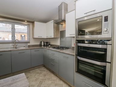A kitchen with grey and white cabinets a gas stove a microwave an oven a sink and small appliances at The Three Bears Lodge Coniston Drive 11 South Lakeland Leisure Village near Warton