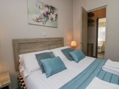 A bedroom with a double bed with blue and gray pillows a bedside lamp and an open door revealing a bathroom at The Three Bears Lodge Coniston Drive 11 South Lakeland Leisure Village near Warton