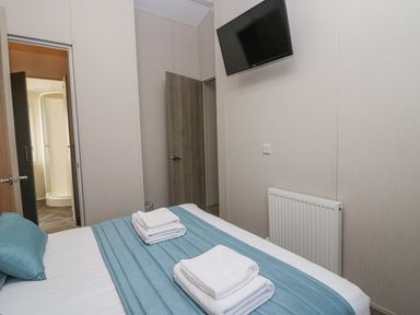 A bedroom with a bed with blue bedding and white towels a wall mounted TV radiator and open doors revealing a bathroom at The Three Bears Lodge Coniston Drive 11 South Lakeland Leisure Village near Warton
