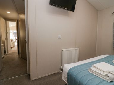 A bedroom with a bed covered with blue bedding towels folded on the bed a wall mounted tv and a radiator at The Three Bears Lodge Coniston Drive 11 South Lakeland Leisure Village near Warton