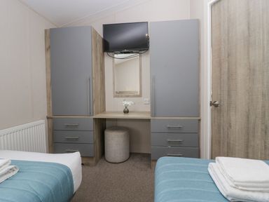 A bedroom with two single beds a vanity desk with a mirror a small stool a wall-mounted television and wardrobes at The Three Bears Lodge Coniston Drive 11 South Lakeland Leisure Village near Warton