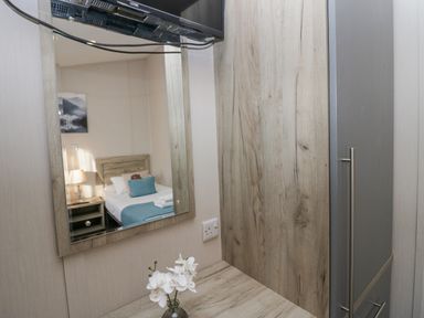 A bedroom with a bed reflected in a mirror above a table with a vase of flowers and a wooden wardrobe at The Three Bears Lodge Coniston Drive 11 South Lakeland Leisure Village near Warton