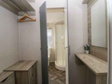 A dressing area with wooden drawers hangers and a small plant beside a bathroom with a shower and toilet at The Three Bears Lodge Coniston Drive 11 South Lakeland Leisure Village near Warton