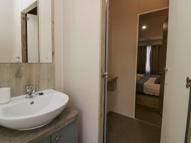 A bathroom sink with a mirror above and a view into a bedroom with a bed and curtains at The Three Bears Lodge Coniston Drive 11 South Lakeland Leisure Village near Warton