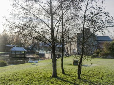 A grassy garden with trees near a pond with swans and a gazebo and buildings in the background at The Three Bears Lodge Coniston Drive 11 South Lakeland Leisure Village near Warton