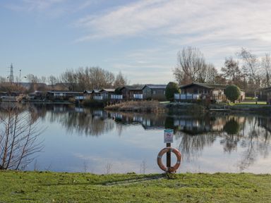 A lake with wooden cabins along the shore and a lifebuoy on the grassy bank at The Three Bears Lodge Coniston Drive 11 South Lakeland Leisure Village near Warton