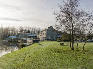 A grassy area with trees a stone building and a small pond with a gazebo at The Three Bears Lodge Coniston Drive 11 South Lakeland Leisure Village near Warton