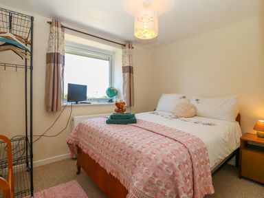 A bedroom with a double bed pink blanket nightstand lamp window with curtains and a clothing rack at Gwynlys in Cemaes Bay